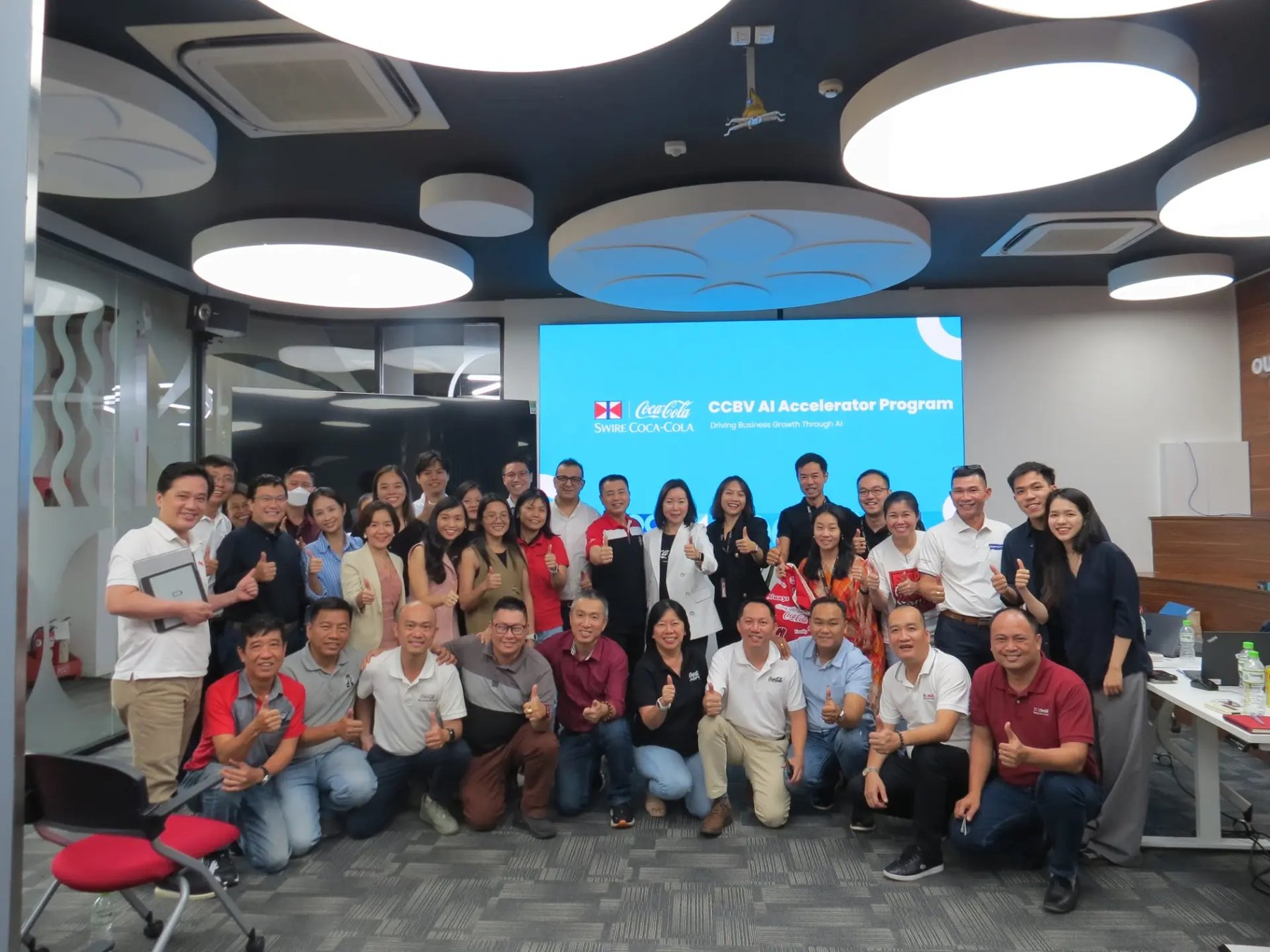 CCBV AI Accelerator Program: Coca-Cola Beverages Vietnam management and department teams together in the training room after the AI deep-dive and idea-generation session, with the programme slide 'Driving Business Growth Through AI' on screen behind them.